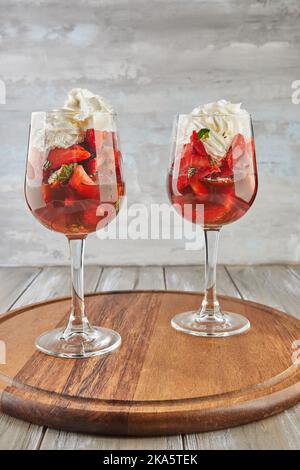 Dessert mit Erdbeeren und Schlagsahne in hohen Gläsern auf Holzhintergrund Stockfoto