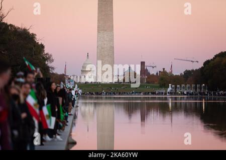 Washington, Usa. 29. Oktober 2022. Das US-Kapitol und das Washington Monument sind in der Ferne sichtbar, wenn Menschen während eines marsches für Mahsa (Zhina) Amini, die junge Frau, die in Gewahrsam der iranischen Moralpolizei starb, eine Menschenkette um den reflektierenden Pool der National Mall bilden. Die Veranstaltung war eine von vielen weltweit, bei der sich in Solidarität mit den Demonstranten im Iran eine Menschenkette bildete. Die Proteste, die bis in die siebte Woche andauern, stellen die größte Bedrohung für das islamische Regime seit Jahrzehnten dar. (Foto von Allison Bailey/SOPA Images/Sipa USA) Quelle: SIPA USA/Alamy Live News Stockfoto