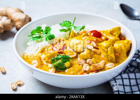 Thailändisches Hühnchen- und Erdnusscure mit Reis in einer weißen Schüssel, grauer Hintergrund. Konzept der asiatischen Küche. Stockfoto