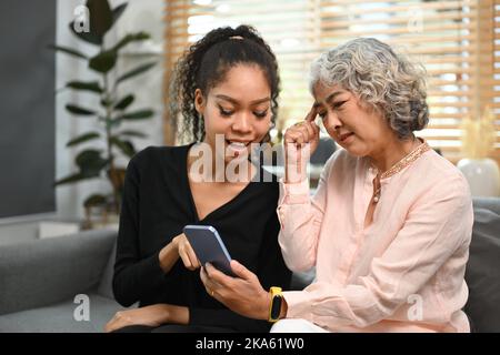 Fürsorgliche Erwachsene Tochter unterrichtet ältere Mutter über soziale Netzwerke auf dem Smartphone. Ältere Menschen, Technologiekonzept Stockfoto