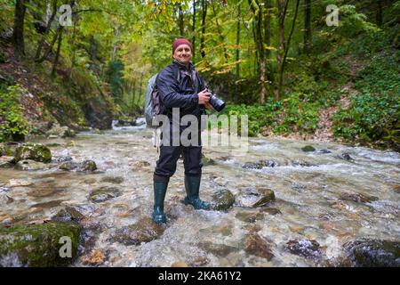 Professioneller Naturfotograf, der an einem regnerischen Morgen Landschaften in einer Schlucht mit einem Fluss fotografiert Stockfoto