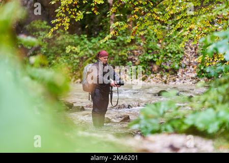 Professioneller Naturfotograf, der an einem regnerischen Morgen Landschaften in einer Schlucht mit einem Fluss fotografiert Stockfoto