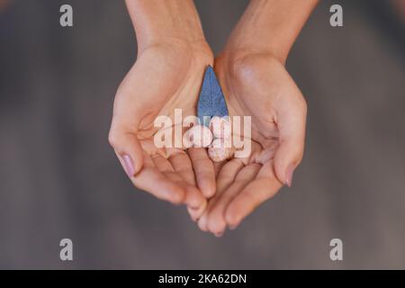 Hält Leben in der Handfläche. Eine unkenntliche Frau hält gesprenkelte Eier und ein blaues Blatt vor grauem Hintergrund. Stockfoto