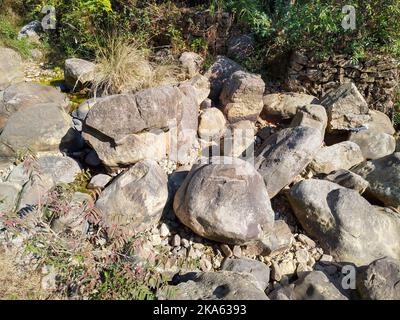 Trockenes Flussbett gefüllt mit großen Rollsteinen mit Bergen im Hintergrund. Himalayan Region Uttarakhand Indien. Stockfoto