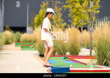 Nettes Mädchen im Vorschulalter, das mit der Familie Minigolf spielt. Glückliches Kind, das Spaß mit Aktivitäten im Freien hat. Sommersport für Kinder und Erwachsene, im Freien Stockfoto