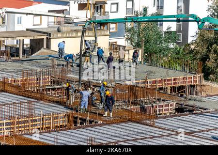 Gießen einer Betonplatte auf einer Baustelle mit Kränen und Gussrohren, chinesische und schwarzafrikanische Arbeiter auf dem Stahlbetondach. Stockfoto