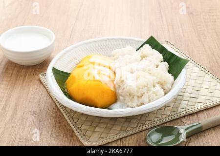Mango mit Sticky Rice, thailändisches Dessert. Serviert auf weißem Teller auf hölzernem Hintergrund Stockfoto