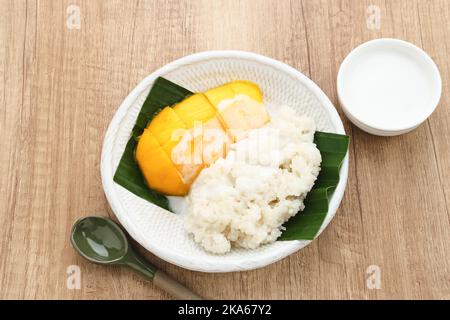 Mango mit Sticky Rice, thailändisches Dessert. Serviert auf weißem Teller auf hölzernem Hintergrund Stockfoto