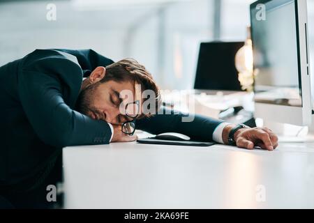 Nach der ganzen Arbeit braucht er eine Pause. Ein müder junger Geschäftsmann schläft tagsüber auf seinem Schreibtisch im Büro. Stockfoto