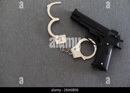 Schwarze Pistole und Metallhandschellen liegen auf dem schwarzen Hintergrund. Private Detektivarbeit. Informationen werden gesucht. Verbrechen und Raub, Gefängniskonzept. Stockfoto