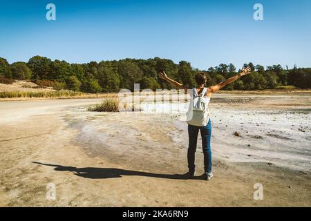 Junge Frau, die in die Solfatara di Manziana (schwefelhaltiges Gebiet) in Italien geht. Die Frau öffnet ihre Arme als Gefühl der Freiheit. Stockfoto