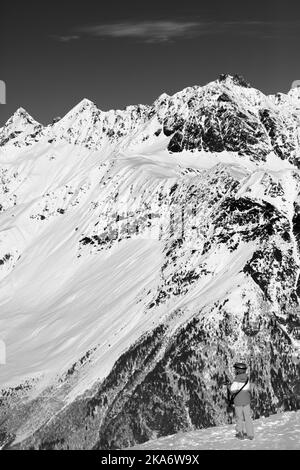 Der kleine Skifahrer macht am schönen Sonnentag Fotos auf den verschneiten Bergen. Kaukasusgebirge im Winter, Svaneti Region von Georgien. Schwarz-weiß getönte ima Stockfoto