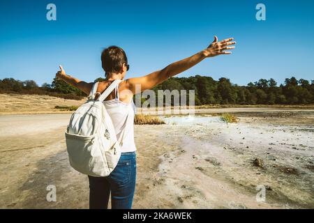 Junge Frau, die in die Solfatara di Manziana (schwefelhaltiges Gebiet) in Italien geht. Die Frau öffnet ihre Arme als Gefühl der Freiheit. Stockfoto