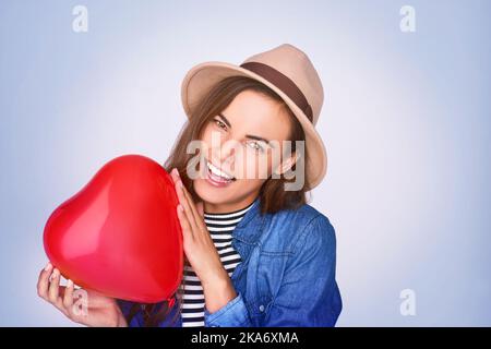 Liebe macht die Welt umrunden. Studioaufnahme einer schönen jungen Frau, die vor einem violetten Hintergrund posiert. Stockfoto