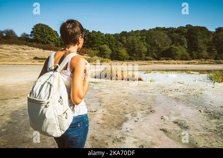 Junge Frau, die in die Solfatara di Manziana (schwefelhaltiges Gebiet) in Italien geht. Die Frau ist von hinten und sie bewundert die Landschaft. Stockfoto