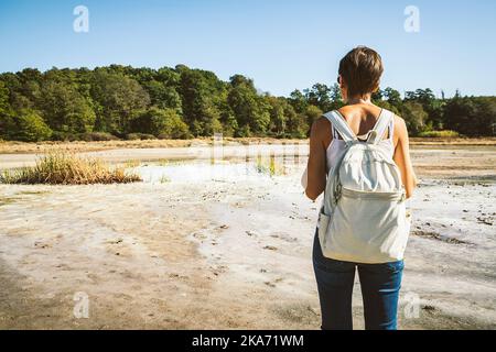 Junge Frau, die in die Solfatara di Manziana (schwefelhaltiges Gebiet) in Italien geht. Die Frau ist von hinten und sie bewundert die Landschaft. Stockfoto