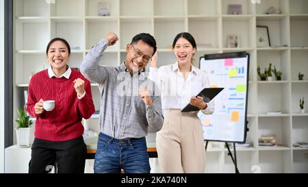 Eine Gruppe von überglücklich asiatischen Geschäftsleuten oder Startup-Mitarbeitern feiert gemeinsam im Büro ihren Erfolg. Stockfoto