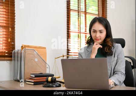 Eine professionelle und nachdenkliche, tausendjährige asiatische Anwältin oder Unternehmensberaterin Hand am Kinn, während sie pensiver an ihrem Fall denkt und arbeitet, Stockfoto