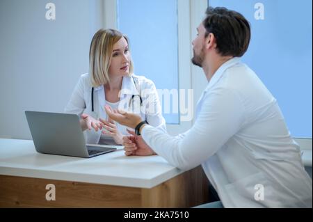 Zwei Menschen in Laborkittel diskutieren etwas und schauen interessiert Stockfoto