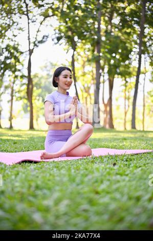 Porträt, entspannt und ruhig junge asiatische Frau in Sportkleidung üben Yoga im grünen Park, Lotus Twist Pose. Wohlfühlkonzept Stockfoto