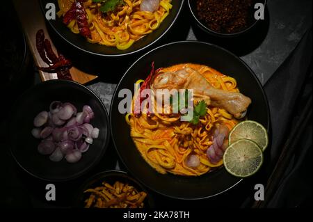 Blick von oben, traditionelles nordthailändisches Speisekonzept, leckere und schmackhafte, würzige cremige Kerrosuppe mit Hühnchen- und Eiernudeln oder Khao Soi Kai. Stockfoto