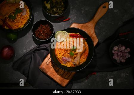 Draufsicht auf ein leckeres Thai-Ei-Nudeln mit Hähnchendrumstick und Gemüse auf dem Tisch mit Gewürzen. Khao Soi Kai Stockfoto