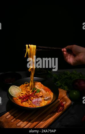 Eine Frau, die Essstäbchen verwendet, um ihre Khao Soi Kai oder Northern Thai-Nudeln mit Hähnchendrumstick und Gemüse zu essen. Nahaufnahme Stockfoto