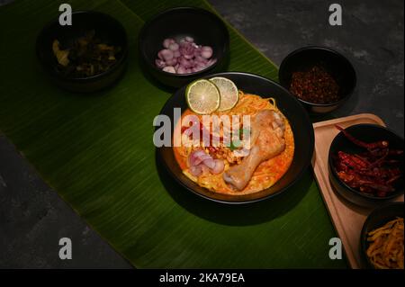 Eine Schüssel mit Khao Soi Kai oder cremig-würziges gelbes Kerri mit Hähnchendrumstick mit Kopierfläche auf Bananenblatt. Draufsicht Stockfoto