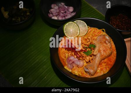 Khao Soi Kai, Noodles-Kurrensuppe mit Hühnerdrumstick, Eiernudeln, gebratenen Chilischoten, Limetten- und Schalottenrutschen auf Bananenblatt. Draufsicht Stockfoto
