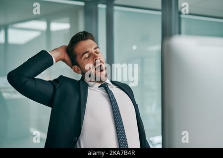 Ich muss meine Augen ein wenig ruhen. Ein müder junger Geschäftsmann, der sich beim Gähnen mit geschlossenen Augen im Büro ausdehnt. Stockfoto