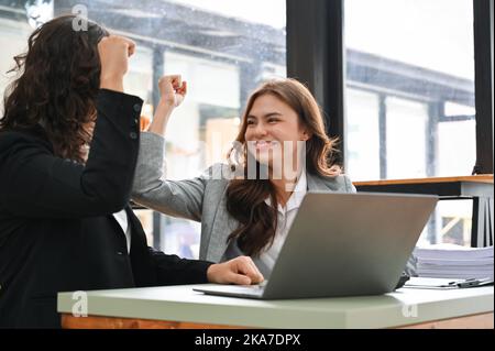 Attraktive und fröhliche junge kaukasische Geschäftsfrau lächelt und feiert ihren Projekterfolg mit ihrem Kollegen im Büro. Gewinnen, Sieg, Stockfoto