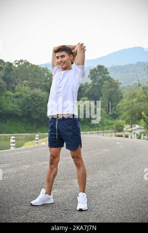 Ein portraitischer, hübscher und athletischer junger asiatischer Mann in Sportkleidung, der seine Arme streckt und sich vor dem Training im Freien aufwärmt. Stockfoto