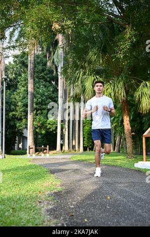 Portrait, Sportliche Passform und hübscher Millennial Asian Mann in Sportswear Laufen in den schönen grünen Park am Morgen. Stockfoto