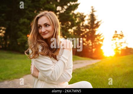 Glückliches Mädchen, das sich bei Sonnenuntergang mit Liebe umarmt. Schöne Frau in der Natur. Das Konzept der Selbstachtung, der Lebenseinstellung. Stockfoto