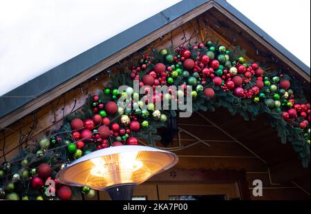 Stilvoll dekorierte Fassade eines Holzhauses für das neue Jahr mit Girlanden, Christbaumzweigen und Bällen. Gemütliche weihnachtliche Atmosphäre. Festliche Stimmung Stockfoto