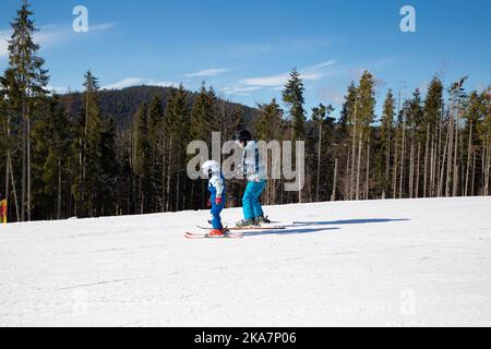 Der kleine Junge lernt während der Winterferien an einem sonnigen, kalten Tag mit seinem Vater in verschneiten Bergen Ski zu fahren. Familie interessanter Zeitvertreib, gesunder Lebensstil. Stockfoto