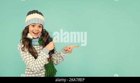 Stauned Kind mit lockigen Haaren in Hut und Schal. Teen Mädchen auf blauem Hintergrund. Porträt des Kindes trägt warme Kleidung. express positive Emotion. Winter fa Stockfoto