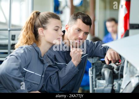 Mechanikerin, die die Auszubildende unter der Motorhaube des Autos zeigt Stockfoto