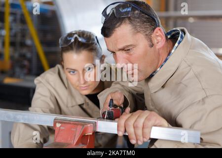 Junge fleißige, effiziente Arbeiterin, die in der Fabrik Metall schneidet Stockfoto