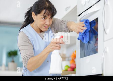 Reife Frau Reinigung Backofen zu Hause Stockfoto