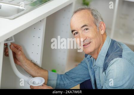 Senioren, die an Rohren unter dem Spülbecken arbeiten Stockfoto