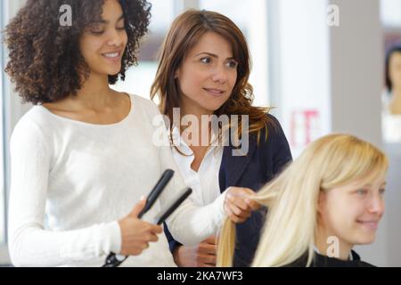 Friseurlehrling bügeln die Haare des Kunden Stockfoto