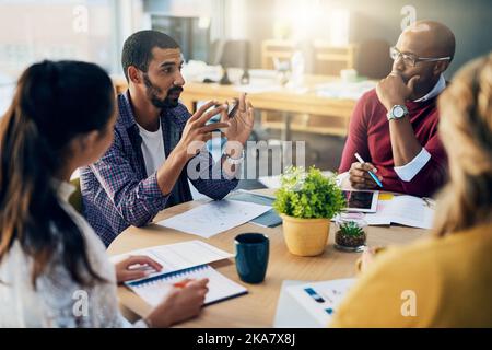 Ein gutaussehender Geschäftsmann, der sich während einer Sitzung in ihrem Sitzungssaal an seine Kollegen wendet. Stockfoto