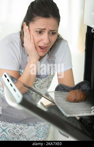 Junge Küchenchefin, die mit frustrierter Gesichtsausdruck in den Ofen schaut Stockfoto