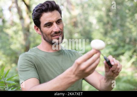 Mann mit einem Messer, der im Wald einen Pilz schneidet Stockfoto
