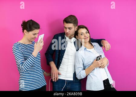Diverse Teenager, die ihr Smartphone benutzen, während sie vor einem rosa Hintergrund für ein Studiofoto posieren Stockfoto