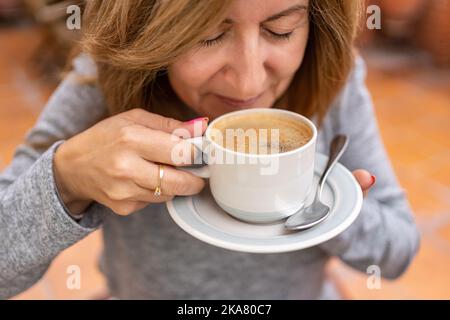 Frau hält eine Tasse frisch gebrühten Kaffee, während sie den Duft von Kaffee riecht. Stockfoto