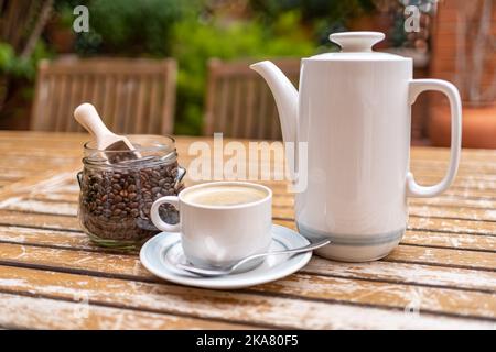 Kaffeeset mit Kaffeemaschine, Tasse und Glas mit Kaffeebohnen auf einem Holzgartentisch. Stockfoto