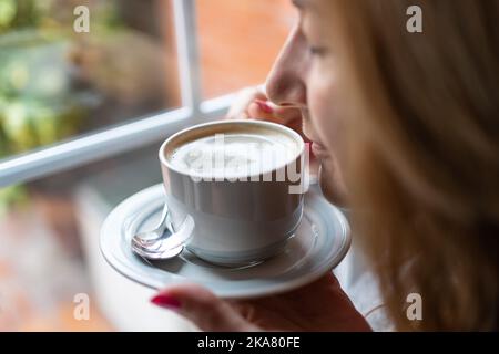 Frau hält eine Tasse Kaffee und riecht dabei den Duft von frisch gebrühtem Kaffee. Stockfoto