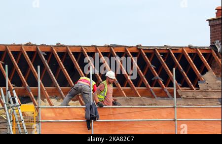 Arbeiter, die ein neues Dach für eine Wohnung aufbauten. Dachdecker wieder Fliesen ein Haus. Stockfoto